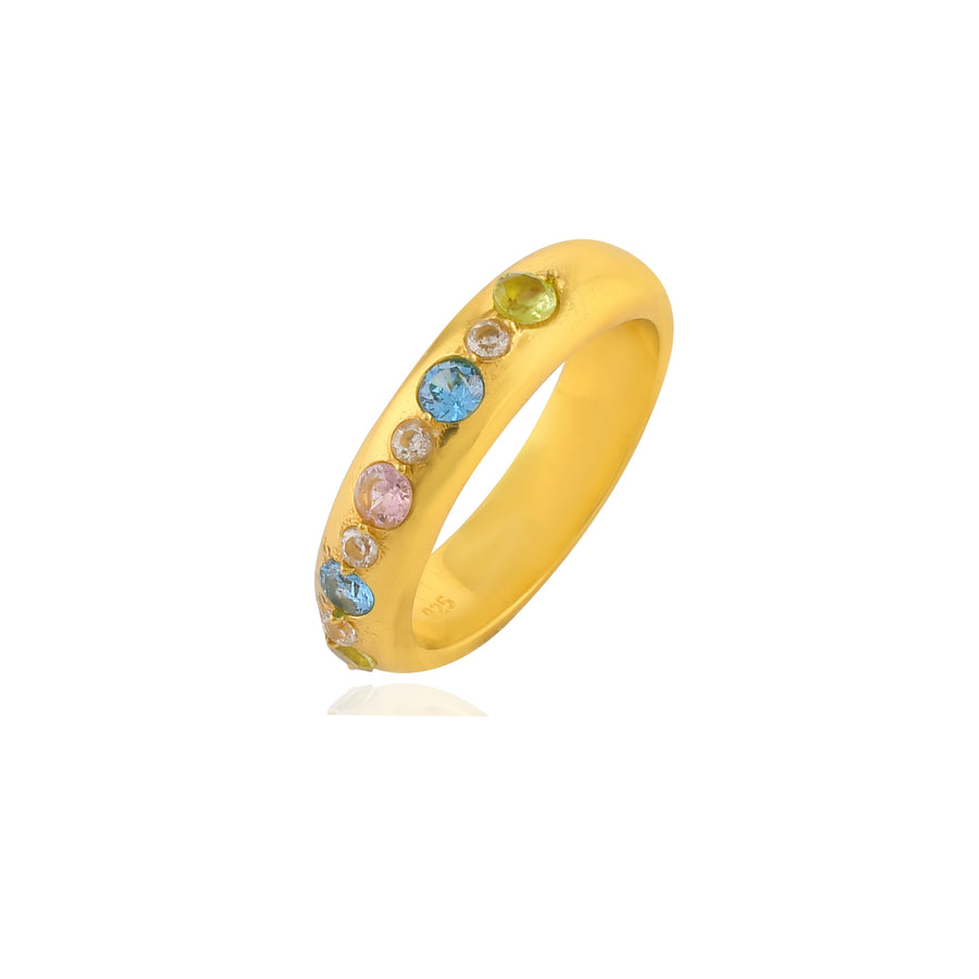 The Tasha Ring, crafted from 22 carat gold, features a delicate band adorned with an array of blue, pink, and green gemstones arranged in a line. This hypoallergenic jewelry piece by Shyla is beautifully displayed against a plain white background.