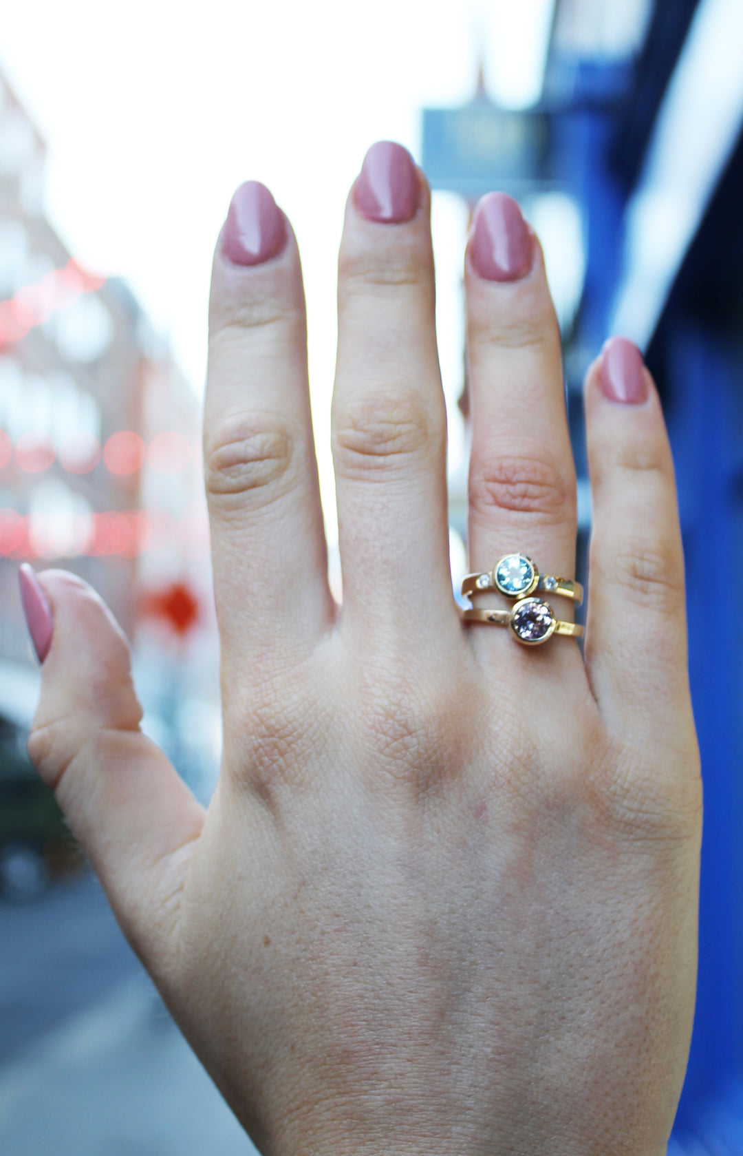 9ct yellow gold ring with aquamarine in gold bezel with small inlaid diamond on either side. Band is flat and 3mm in width. Shown alongside pink tourmaline ring, on ring finger.