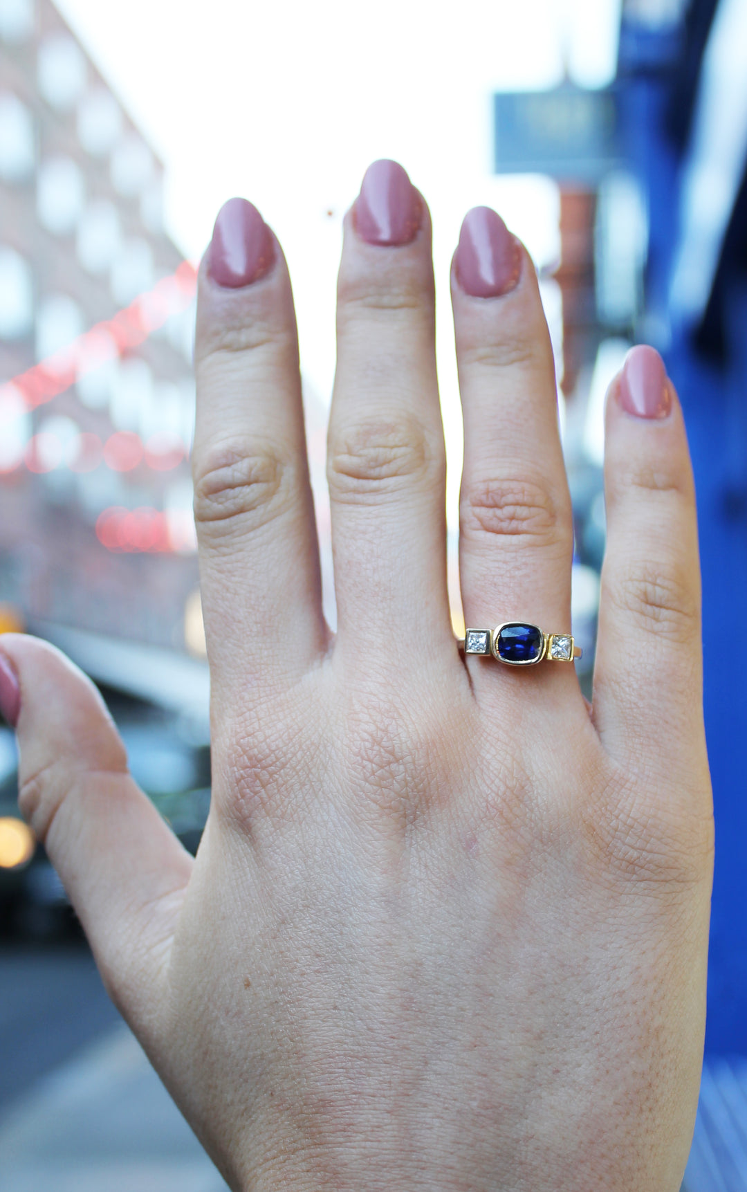 18ct yellow gold ring round sapphire in centre set in 18ct gold with square diamond on either side. Band is 1.75 mm wide. Shown here on a ring finger.