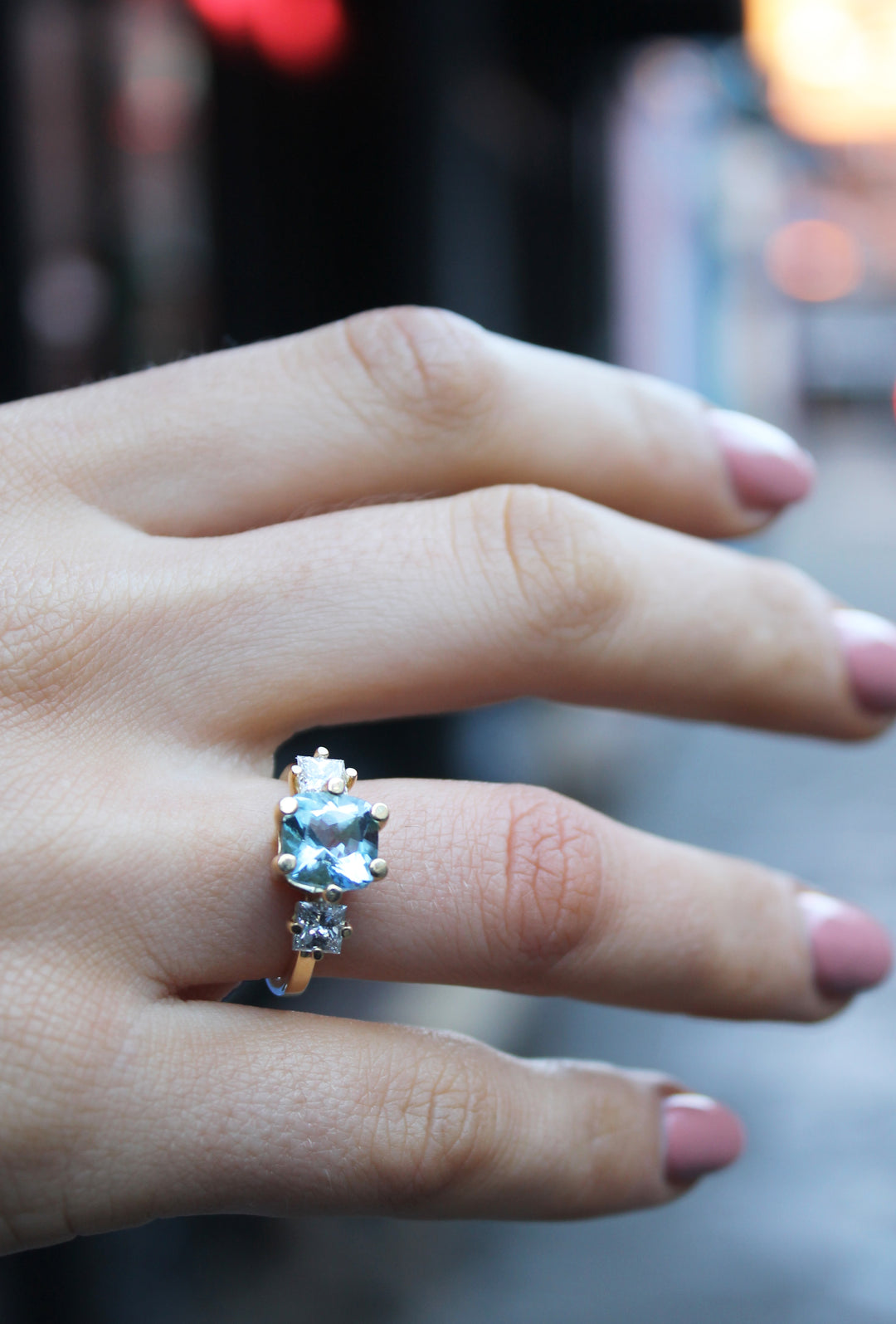 18ct yellow gold ring band is 2.3mm wide. 8x8mm square aquamarine in the centre with a square diamond on either side all in a basket setting. Shown here tried on, on a ring finger