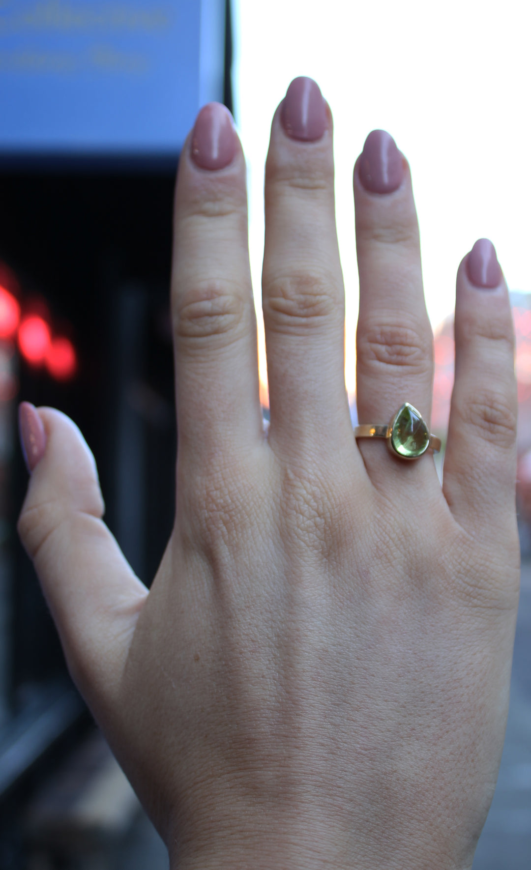 9ct yellow gold ring with a teardrop shaped peridot cabochon, which is a moss green gem, in a bezel setting. The band is flat in shape and is 3mm wide. The 9ct yellow gold band is 3mm wide. Shown here on a ring finger