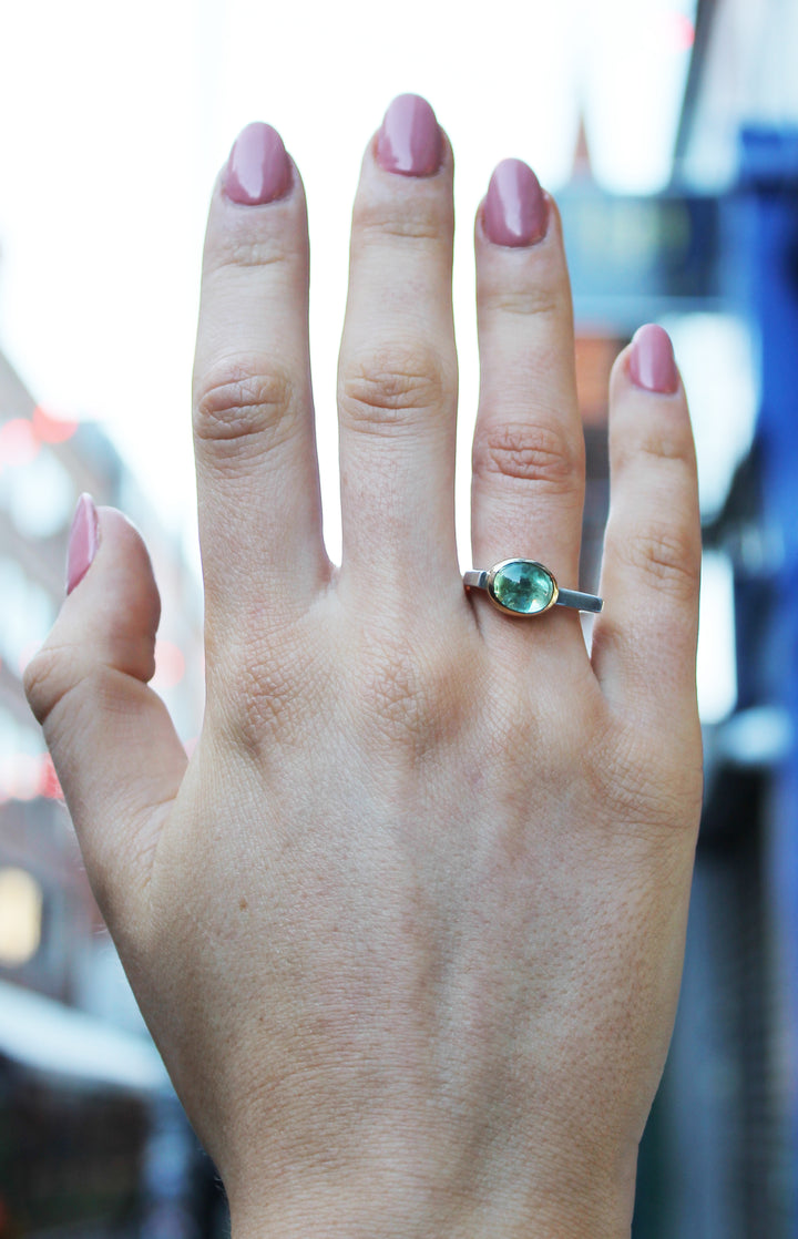 Silver ring with green tourmaline in 9ct yellow gold bezel . Tourmaline is off centre. The top of the ring is rectangular making the band D shaped. Shown here on a ring finger.