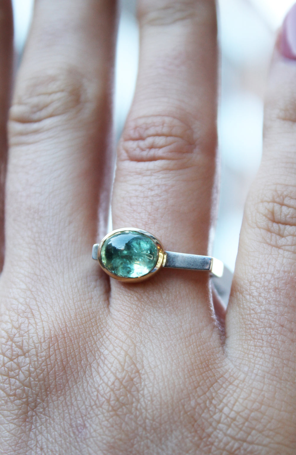 Silver ring with green tourmaline in 9ct yellow gold bezel . Tourmaline is off centre. The top of the ring is rectangular making the band D shaped. Shown here on a ring finger.