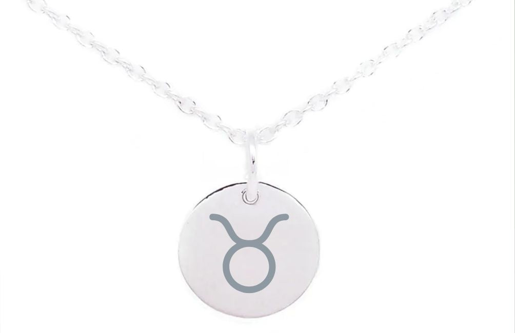 A sterling silver necklace featuring a round pendant with the Taurus zodiac sign engraved on it. The pendant, our Personalised Charms Horoscope Large Disc Charm Silver, hangs from a fine, twisted chain. The background is plain white.