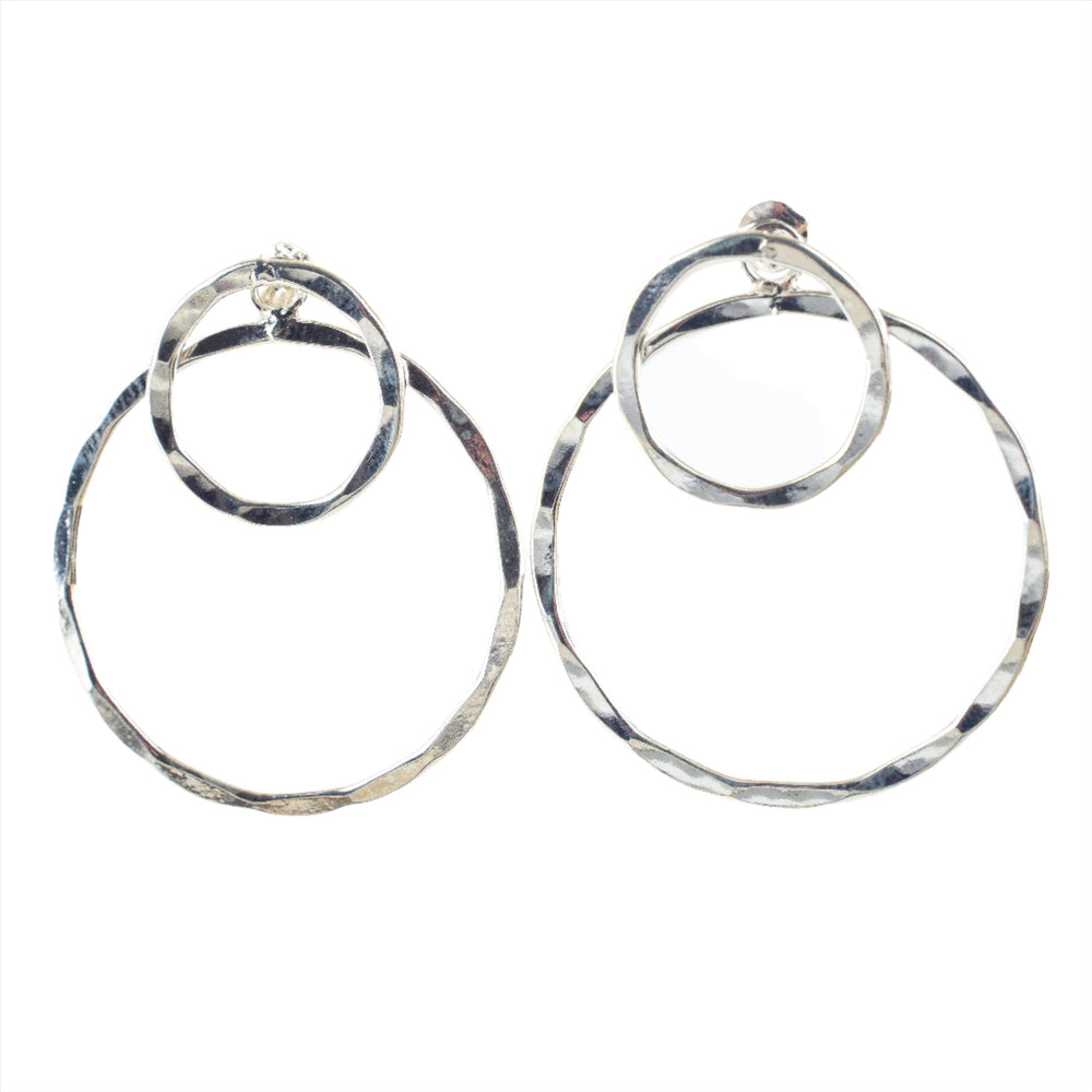 Introducing the Double Circle Earrings from Watermelon Tropical: These sterling silver earrings feature a modern design with two interlocking hammered metal rings. The smaller ring attaches to the earlobe, while the larger ring dangles below, perfecting a contemporary and stylish look. Available in both silver and gold options, these concentric circle earrings boast a rustic texture for a unique touch.