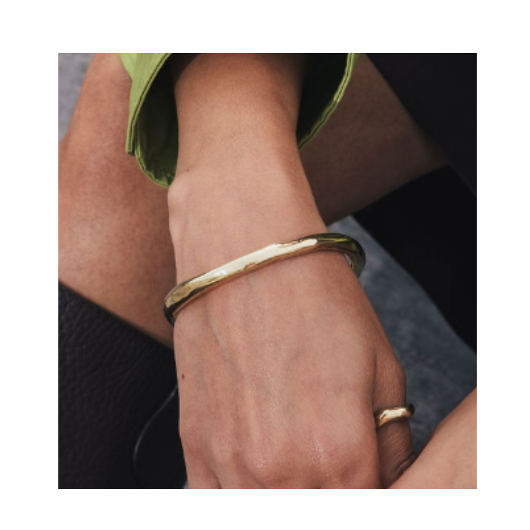 A close-up of a hand wearing the Thorn Bangle by Madeleine Blaine, paired with a hand-carved ring. The person, dressed in a green sleeve and black garment, showcases this unique piece that evokes contemporary Dublin style.