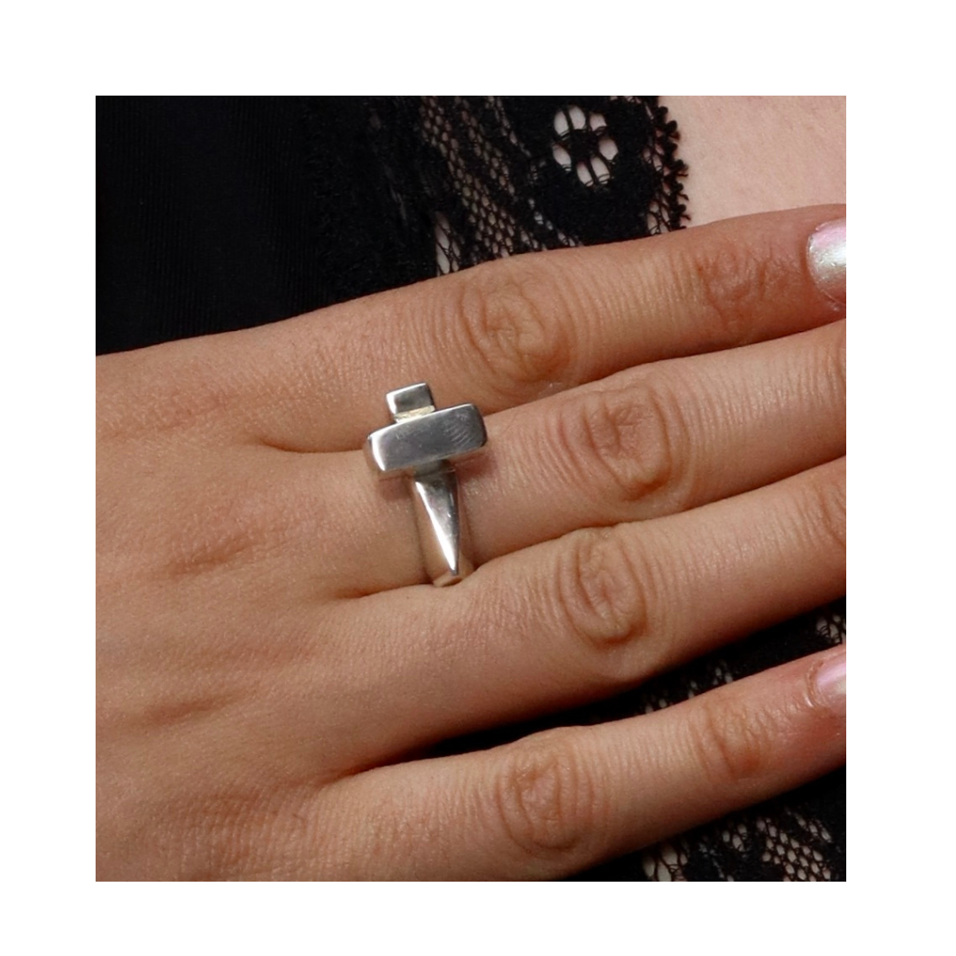 A hand wears the Totem Ring in Silver by Madeleine Sculptural Jewellery, a handmade cross-shaped silver ring, with a black lace garment in the background.