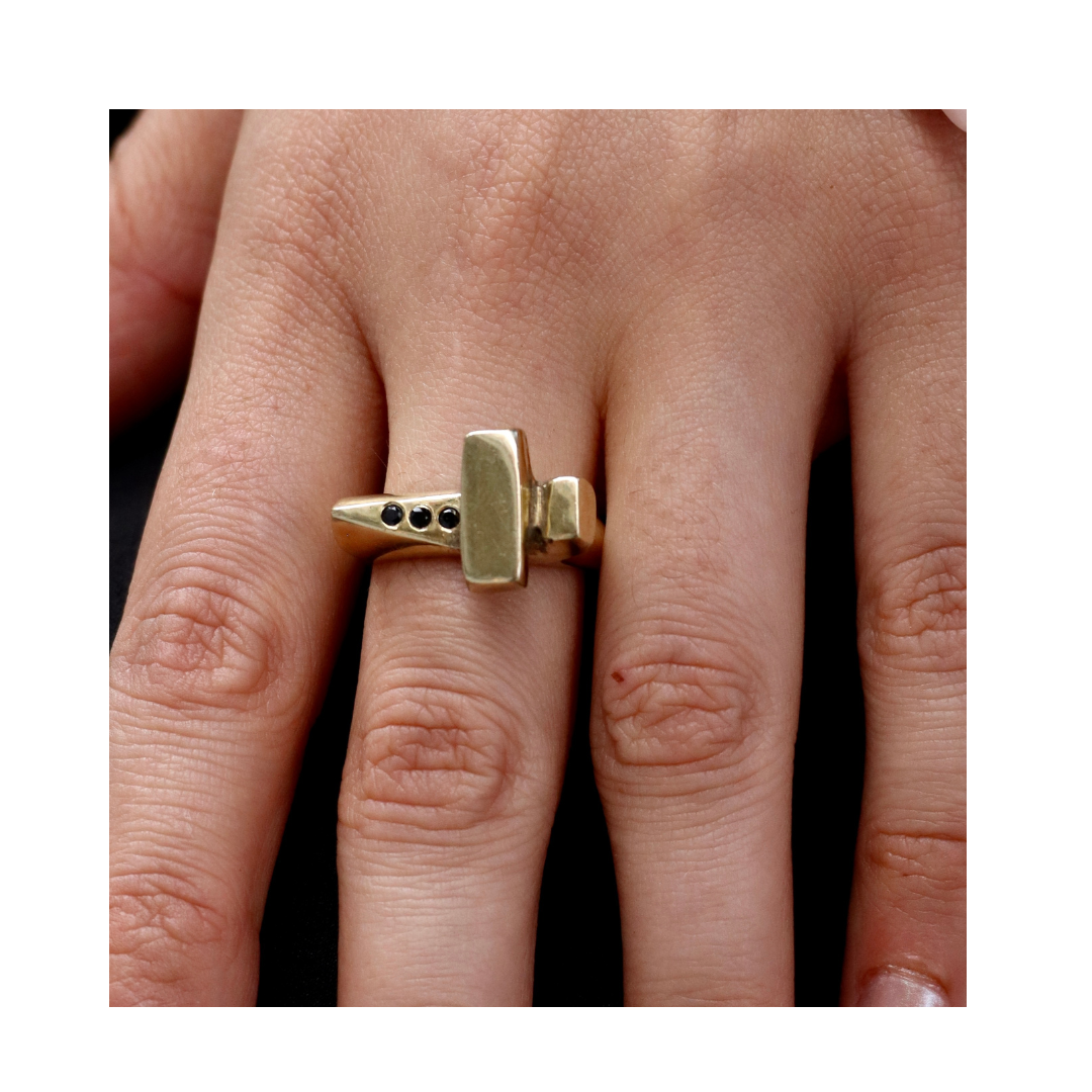 A close-up of a hand wearing the Totem Ring with Black Spinel by Madeleine Sculptural Jewellery—a bold, handmade gold ring shaped like a hammer, set with black stones on the handle.