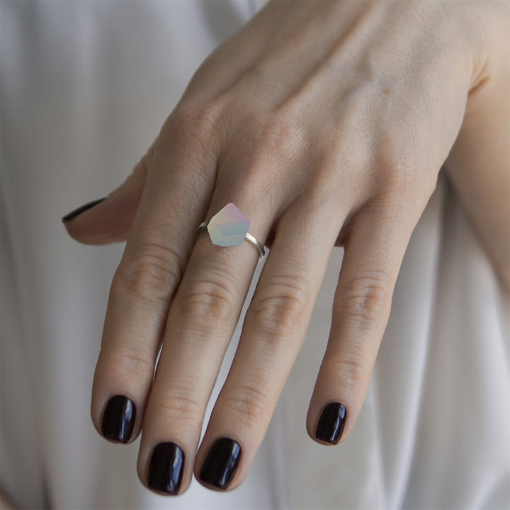 A hand with dark purple nail polish wears the Fruit Bijoux Ring Top Unicorn by Fruit Bijoux—a sterling silver ring set with a pastel geometric stone—shown against a soft, light background.