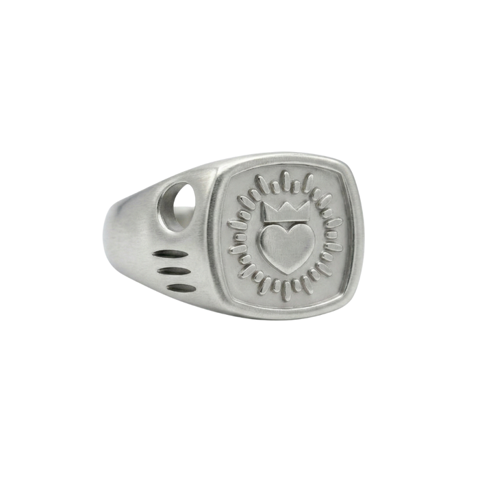 The Collective Dublin's Keith Haring Inspired Claddagh Ring is a handmade silver signet featuring an engraved heart with a crown and radiating rays on a rounded square face, with decorative cutouts—a modern take on timeless Irish jewelry.