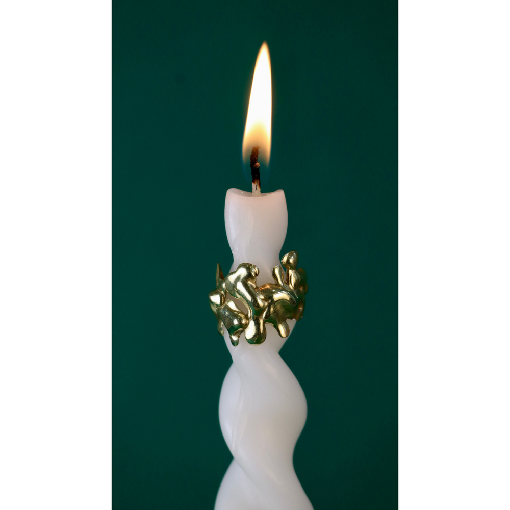 The Molten Ring by Madeleine Sculptural Jewellery is a white twisted candle featuring a gold recycled brass ring, burning brightly against dark green—evoking sustainable elegance and handcrafted style.