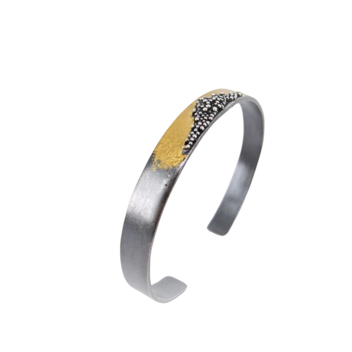 A sleek, silver-toned cuff bracelet with a hammered texture, featuring a 24 kt yellow gold accent and a cluster of small silver beads on one side, the **Oxidised Etrusc Bracelet** by **MarCucurella**.