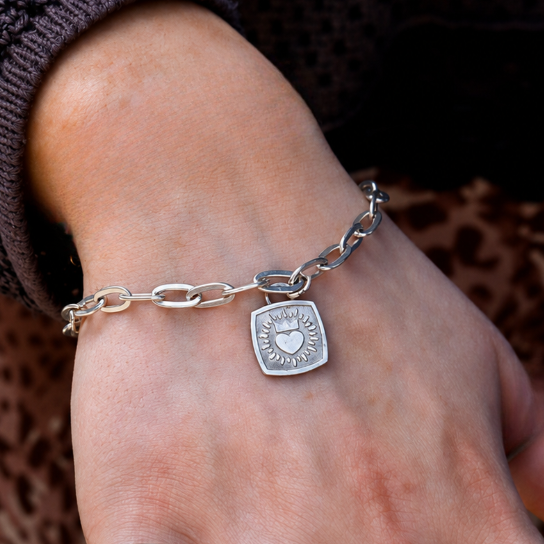 A close-up of a hand wearing The Collective Dublin’s Keith Haring Inspired Claddagh Paper Clip Chain Bracelet, paired with a brown knitted sweater for a stylish and modern take on classic Irish jewelry.
