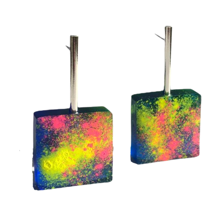 A pair of square-shaped Graffiti Block Earrings by Angela O'Keefe featuring a vibrant, abstract design with splashes of neon yellow, pink, and green colors on a dark background. These handmade earrings hang from silver rectangular metal hooks.