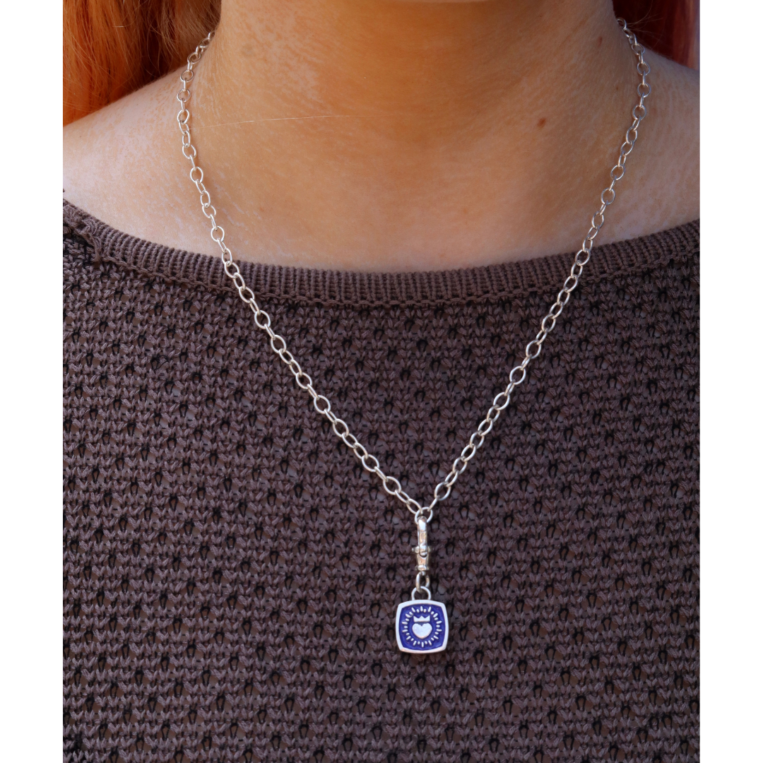 A person wears a brown textured sweater and a silver chain with The Collective Dublin's Keith Haring Inspired Double Sided Enamel Claddagh Pendant—subtle, stylish jewelry referencing the artist’s iconic aesthetic.