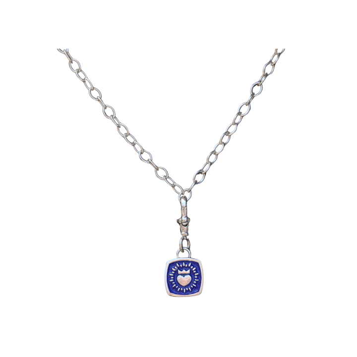 The Collective Dublin’s Keith Haring Inspired Double Sided Enamel Claddagh Pendant features a blue square with a central white heart and radiant lines on a silver chain, shown against a plain white background.