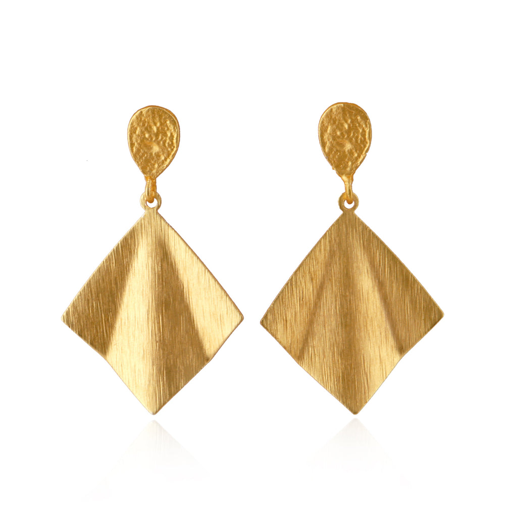 The part that sits on the earlobe is a small, teardrop-shaped piece of metal with a slightly irregular surface. The texture is subtly hammered, giving it a handcrafted, organic look. Hanging from the stud is a large, diamond-shaped pendant with a brushed metal finish. The brushed texture creates a soft, directional pattern on the surface, giving the gold a slightly matte yet reflective appearance. 