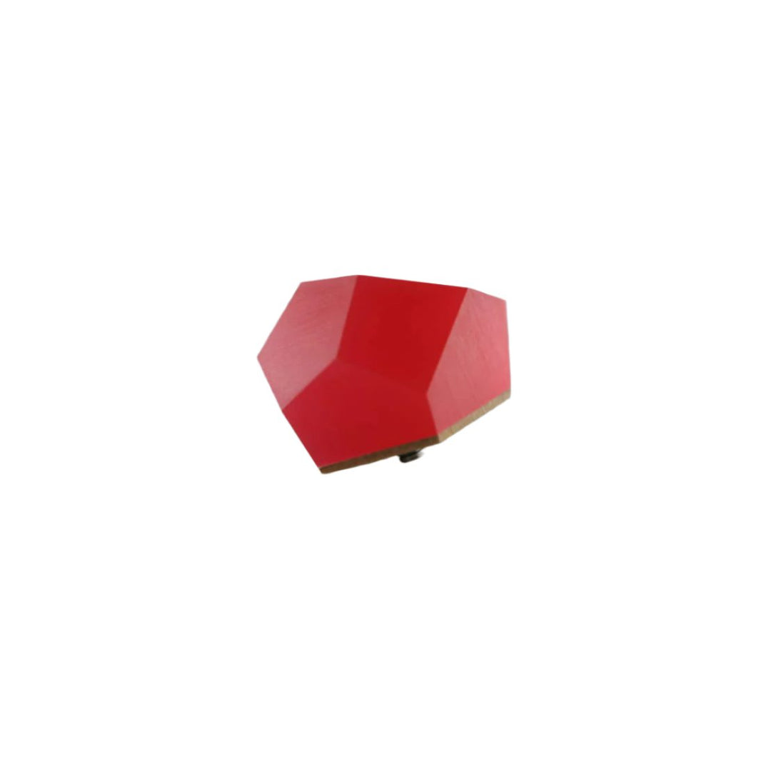 A small, red, irregularly shaped polygon sits on a flat, light gray surface. The shape has a matte finish and appears to be a geometric object or decoration. Its angles and sides are unevenly distributed, creating an abstract appearance reminiscent of the Fruit Bijoux Fruit Bijoux Ring Top VU Crystals Ruby Red.