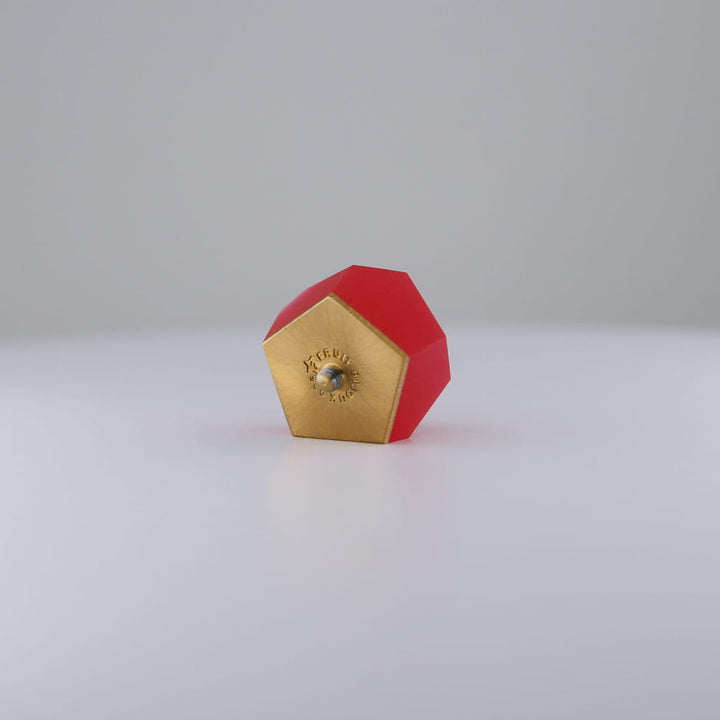 A Fruit Bijoux Ring Top VU Crystals Ruby Red from Fruit Bijoux with a red body and a 24ct gold-plated end lies on a smooth white surface against a light gray background.