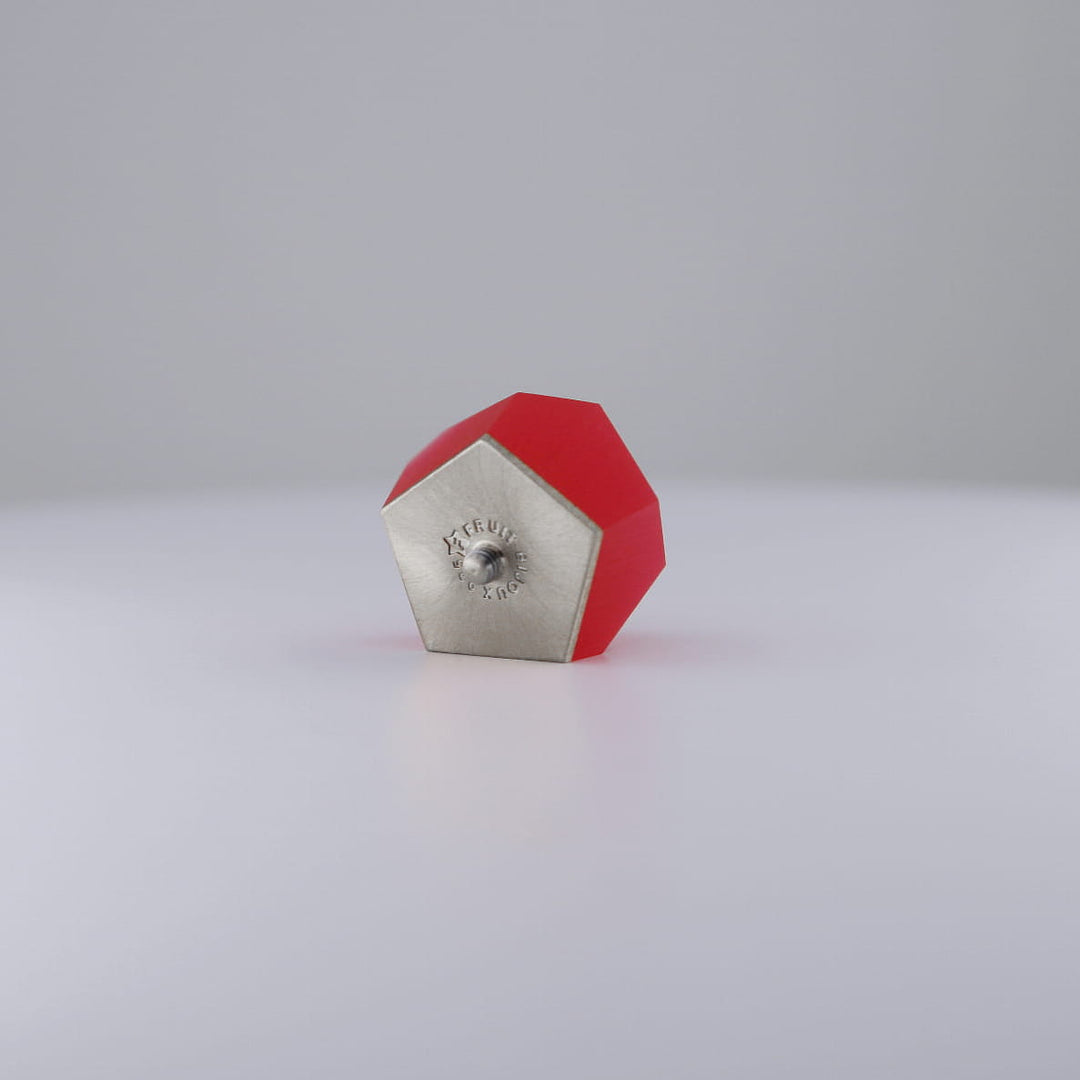 The Fruit Bijoux Ring Top VU Crystals Ruby Red by Fruit Bijoux, with its ruby-red geometric design, sits on a white surface, resembling the sleek style of an interchangeable ring module against a light gray background.