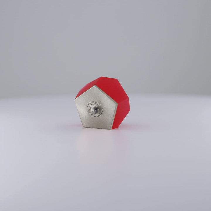 The Fruit Bijoux Ring Top VU Crystals Ruby Red by Fruit Bijoux, with its ruby-red geometric design, sits on a white surface, resembling the sleek style of an interchangeable ring module against a light gray background.