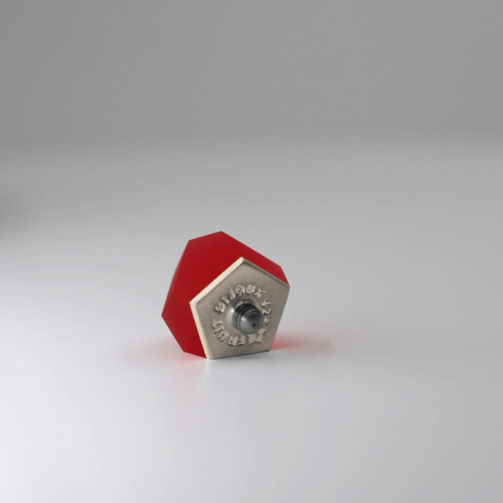 A Fruit Bijoux Ring Top VU Crystals Ruby Red by Fruit Bijoux, with a 24ct gold-plated screw-like center, sits upright on a plain, white surface. The metal piece has engraved text and a central hole, suggesting it may be a specialized component or connector.