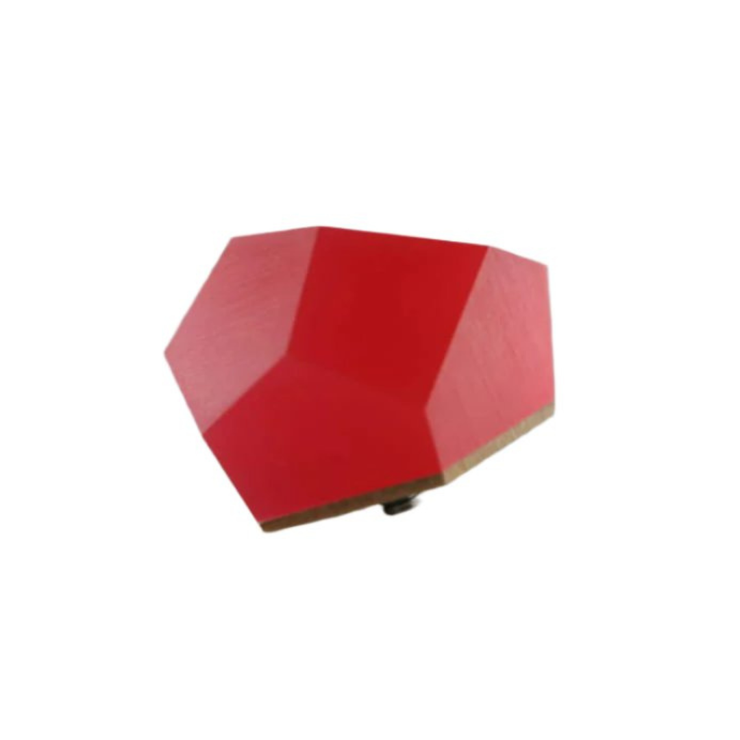A small, red, irregularly shaped polygon sits on a flat, light gray surface. The shape has a matte finish and appears to be a geometric object or decoration. Its angles and sides are unevenly distributed, creating an abstract appearance reminiscent of the Fruit Bijoux Fruit Bijoux Ring Top VU Crystals Ruby Red.