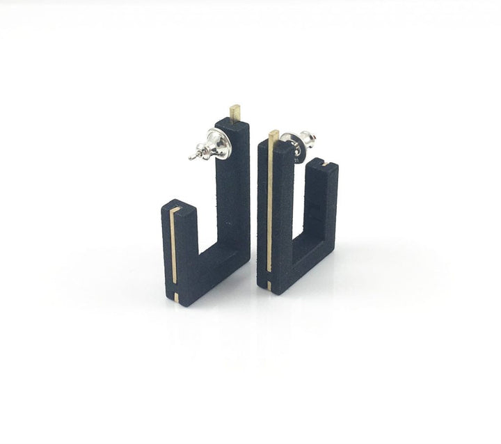 Pair of black geometric earrings with a unique design resembling the letter "L." These Vibe Brutalist Earrings by Elsiem have gold accents on the edges and are secured with silver backings, set on a clean white background.