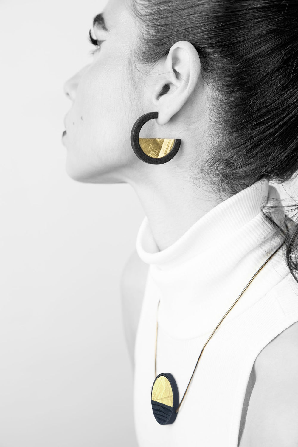 A woman in a sleeveless white turtleneck wears Elsiem’s Vibe Wave Circle Fascia Necklace. She faces left with her hair pulled back, highlighting the bold, modern jewelry.