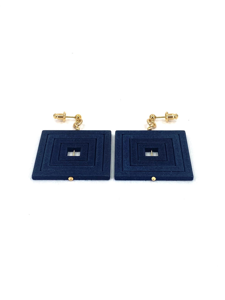 A pair of Elsiem Vibe Decreasing Square Earrings featuring a layered navy blue design with a small metallic accent in the center of each square. The earrings are attached to gold-toned screw-back studs. The background is white.