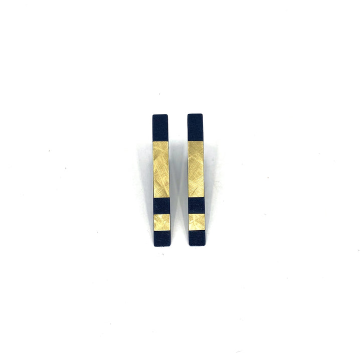 Two rectangular, bold modern Vibe Incomplete Triangle Earrings made of dark blue material with gold accents from Elsiem. Each earring features a gold square at the top and a lacquered brass strip near the bottom, creating a symmetrical and minimalist design against a white background.