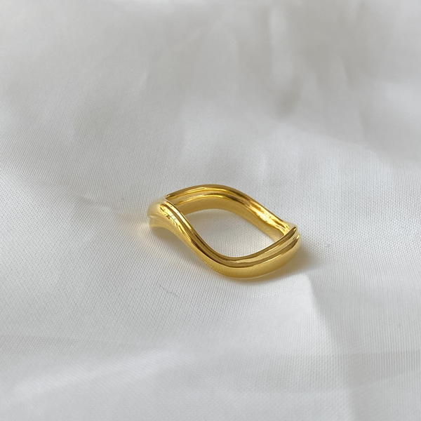 A close-up of a hand-carved ring rests on soft white fabric. The Wabi Ring by Bonvo, made of solid sterling silver with 18ct gold plating, features a unique flowing design with smooth, curved edges and an overall modern aesthetic.