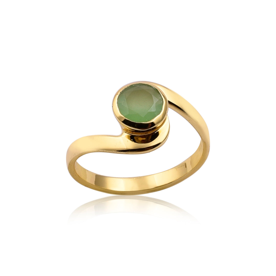 A Chrysophrase Chalcedony Gold Ring with a unique, curved band design, featuring a round, faceted green chrysoprase chalcedony gemstone set in the center by Watermelon Tropical. The ring is positioned against a plain white background, highlighting its elegant and minimalist style.