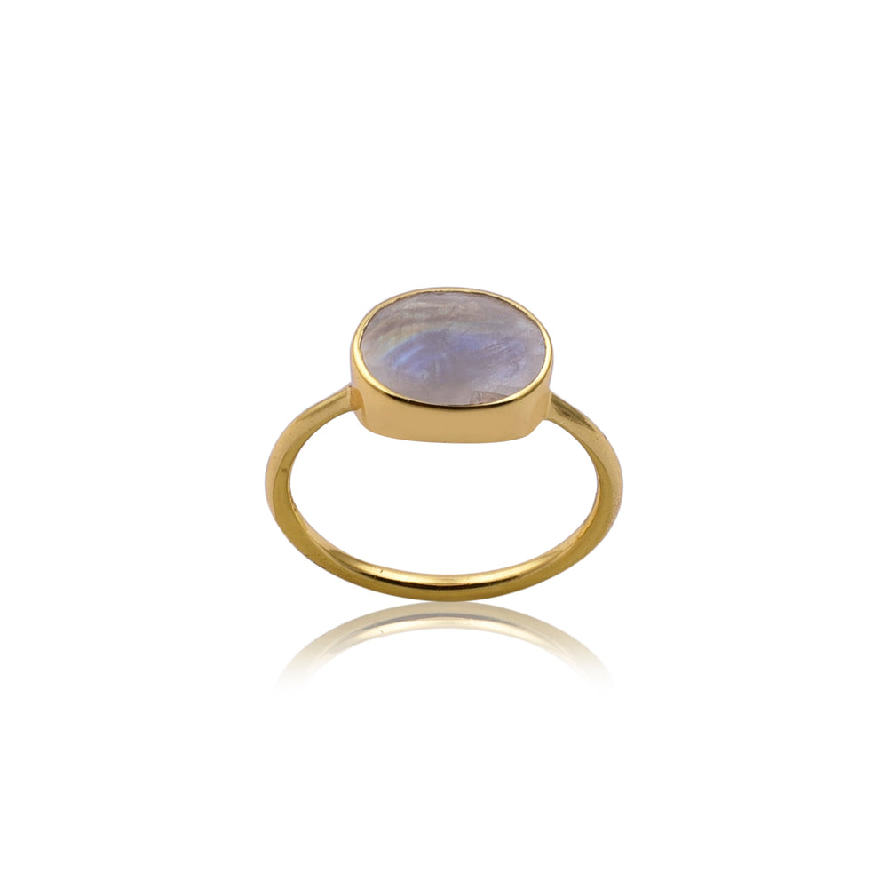 The Oval Rainbow Moonstone Gold Ring by Watermelon Tropical features a smooth, oval-shaped, iridescent rainbow moonstone in the center. The stone displays hues of blue and purple, set in a simple gold band. This piece of handmade jewelry is displayed against a white background with a reflection visible beneath it.