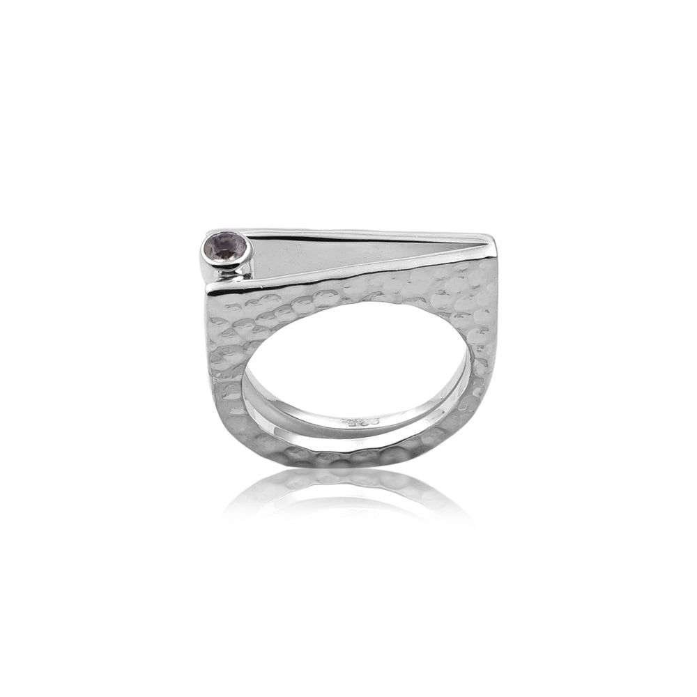 The Silver Bar Rainbow Moonstone Ring by Watermelon Tropical is a modern, sterling silver ring with a unique geometric design. The band features a textured, hammered finish, and a sleek, angular bar extends across the top, holding a small round rainbow moonstone on one end. This piece of handmade jewelry reflects light beautifully, showcasing its detailed craftsmanship.