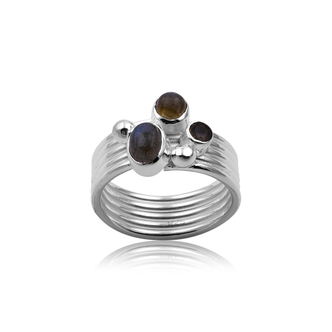 A Triple Labradorite Silver Ring by Watermelon Tropical adorned with three dark labradorite stones of varying sizes and two small silver spheres. The band has a textured, layered design. This piece of handmade jewellery is placed against a white background with a slight shadow beneath it.