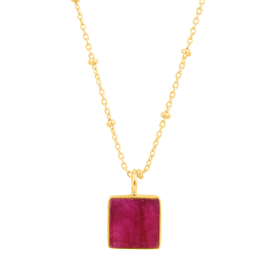 A gold vermeil necklace features a delicate chain adorned with small bead accents. The pendant is a square Rough Ruby gemstone set in a gold frame, hanging at the center. The overall design is elegant and minimalistic. This stunning piece is known as the Wynter Necklace by Watermelon Tropical.