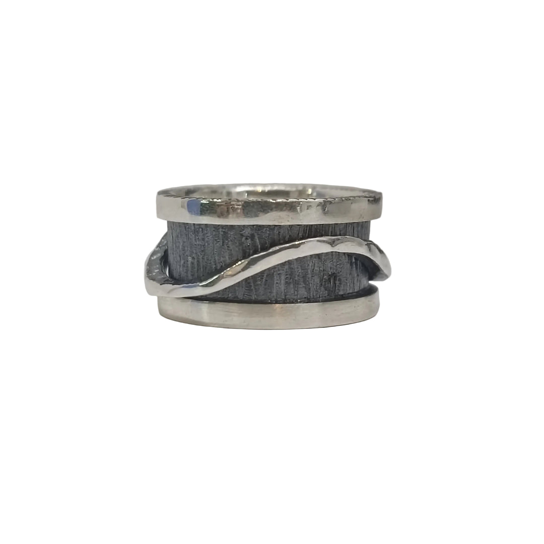 The K.And Wave Spinner Ring features a wide, brushed dark band with a wavy silver strip wrapping around it, creating a striking oxidised look that stands out against light backgrounds.