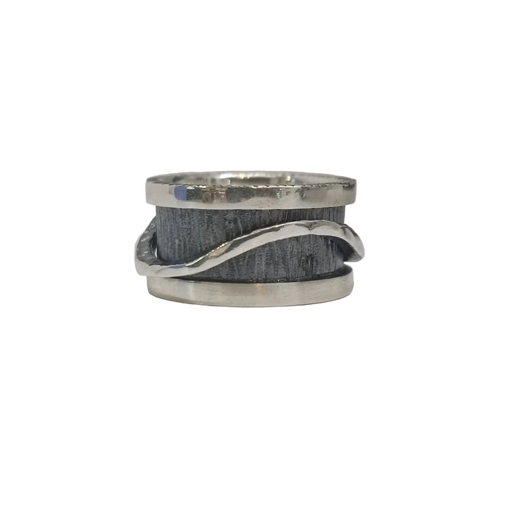 The K.And Wave Spinner Ring features a wide, brushed dark band with a wavy silver strip wrapping around it, creating a striking oxidised look that stands out against light backgrounds.