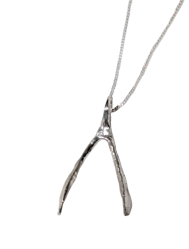 A silver wishbone necklace, resting on a draped white linen fabric.