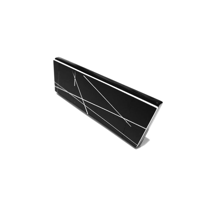 A sleek, black rectangular object with a glossy surface and white abstract lines intersecting across it, resembling the elegance of handmade jewelry. Positioned slightly angled against a plain white background, its unique design highlights a modern and minimalistic appearance — introducing the Zoe Brooch by Alex + Svet.