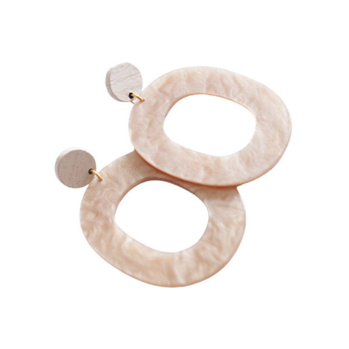 A pair of large, textured earrings made from light, natural upcycled ash wood. Each hand-made earring features a circular stud attached to an irregularly shaped, hollow oval hoop. The gold-plated Acrylic 09 Earrings by Studio Nok Nok have a subtle, pale beige color.