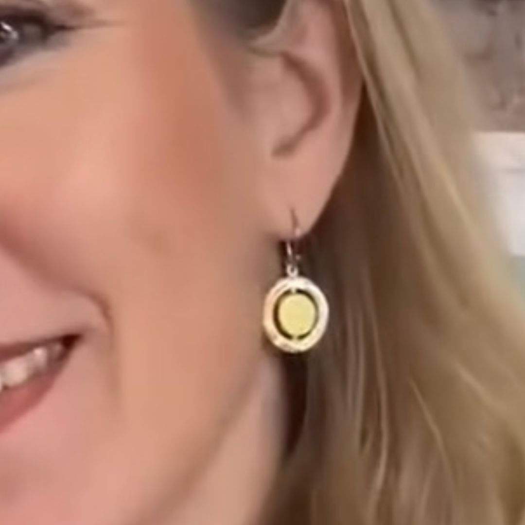 Close-up of a smiling woman with blonde hair, showcasing her ear adorned with Gallardo & Blaine Designs’ Urú Dangle Earring—round sterling silver with a yellow center and silver border.