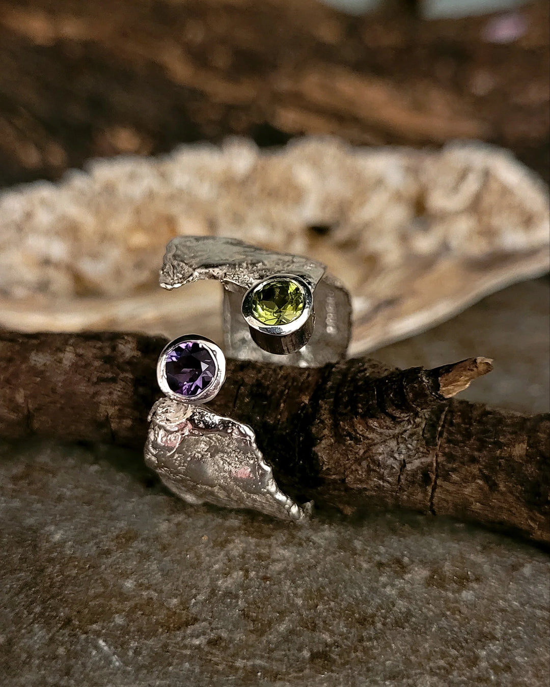 The Amethyst & Peridot Faerie Tale Ring by Caroline Stokesberry-lee showcases a sterling silver adjustable band with organic texture, featuring amethyst and peridot stones set at opposite ends against a natural background.