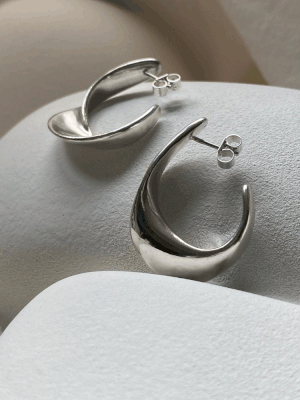 A Moment Large Earrings by Inner Island: modern crescent-shaped silver earrings with a shiny finish and ethical craftsmanship, showcased on a smooth white textured surface.