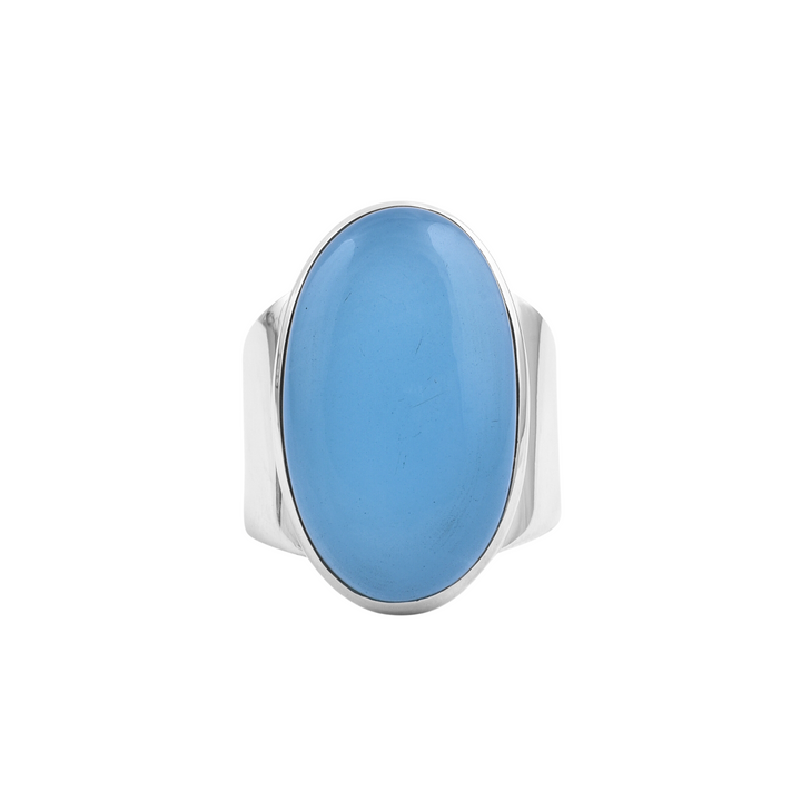 A sterling silver ring features an oval-shaped, smooth aqua chalcedony set in the center. The stone's surface is glossy, reflecting light, and the ring's wide metal band enhances the prominence of the blue stone. The overall design is sleek and modern. Presenting the Aqua Chalcedony Sterling Silver Band by Watermelon Tropical.