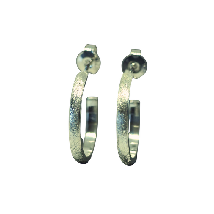 A pair of Ellipse Small Hoops Silver by Aud with a textured, matte finish. Each earring has a post back for securing in pierced ears, making them perfect for everyday wear. The handmade jewelry is shown against a plain white background.