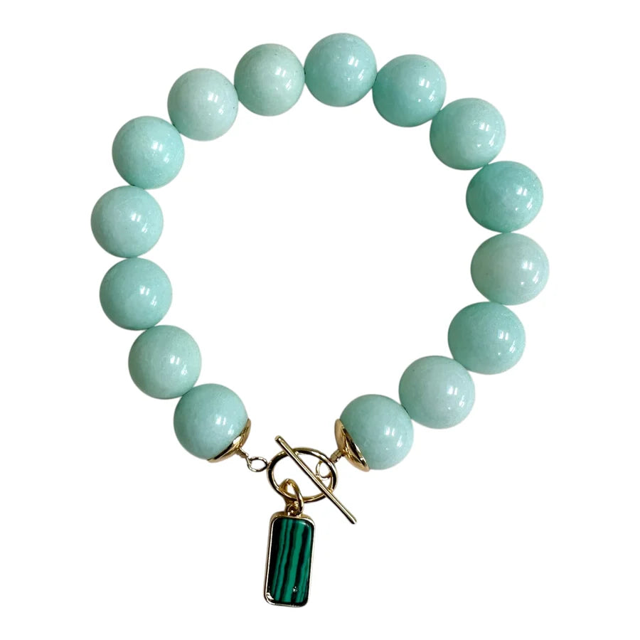 The Azure Bloom Bracelet by Aria V is a handmade piece from Dublin, featuring large, round mint blue chalcedony beads, a gold toggle clasp, and a small rectangular green and black malachite pendant.