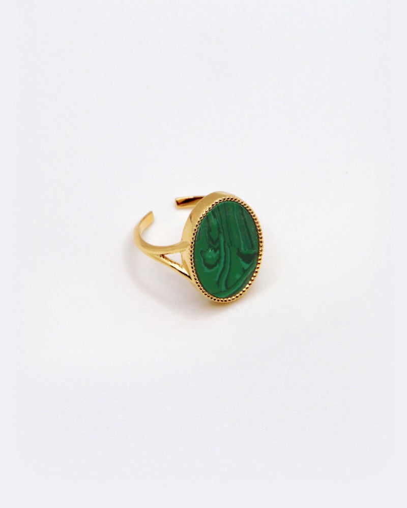 The Frida Ring, designed by Nilai, features a gold open band and an oval-shaped green natural stone in the center. Its polished surface with natural patterns is beautifully showcased against a plain white background.