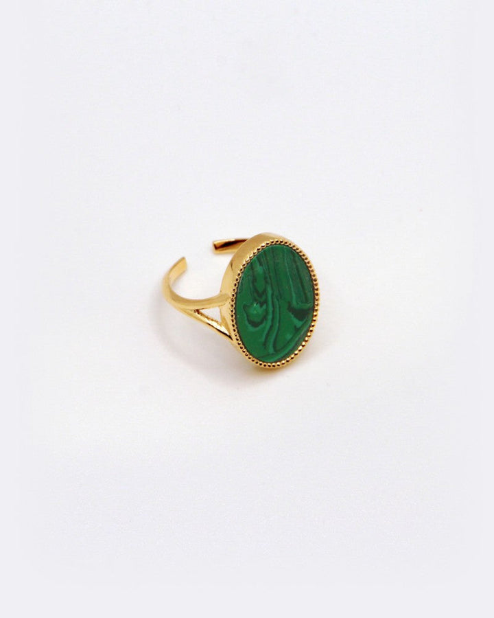 The Frida Ring, designed by Nilai, features a gold open band and an oval-shaped green natural stone in the center. Its polished surface with natural patterns is beautifully showcased against a plain white background.